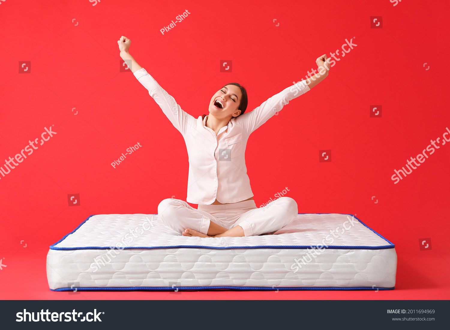 Happy young woman sitting on mattress against color background #2011694969