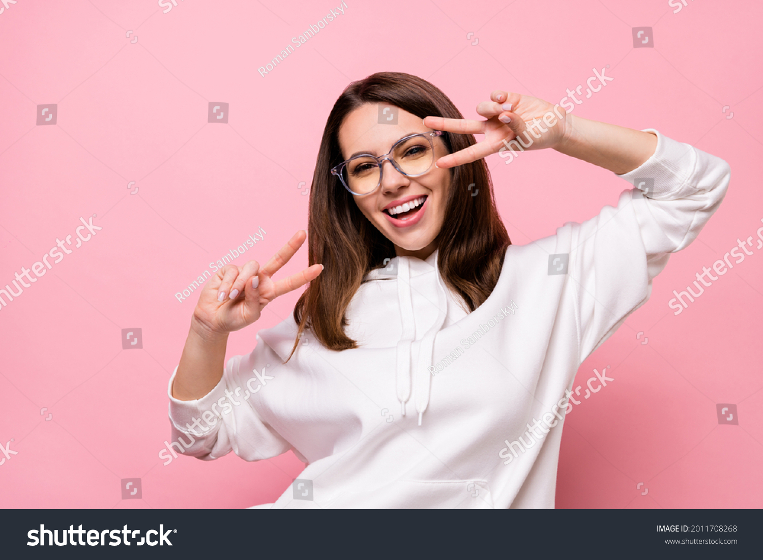 Photo of shiny pretty young lady wear white hoodie glasses smiling v-signs cover eyes isolated pink color background #2011708268
