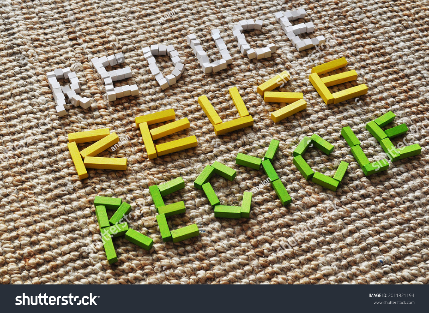 3D diagonal text in colored wooden blocks in white, yellow and green, on a jute carpet. It reads Reduce, Reuse, Recycle. Message for circular economy, sustainability, climate action, climate change. #2011821194