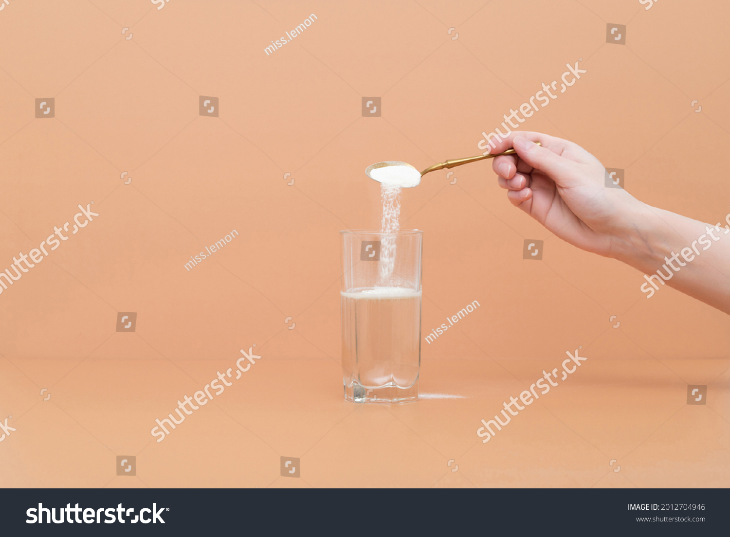 Hand pours collagen protein powder in a glass of water on a beige background. A natural supplement for skin beauty and bone health. Space for text. #2012704946