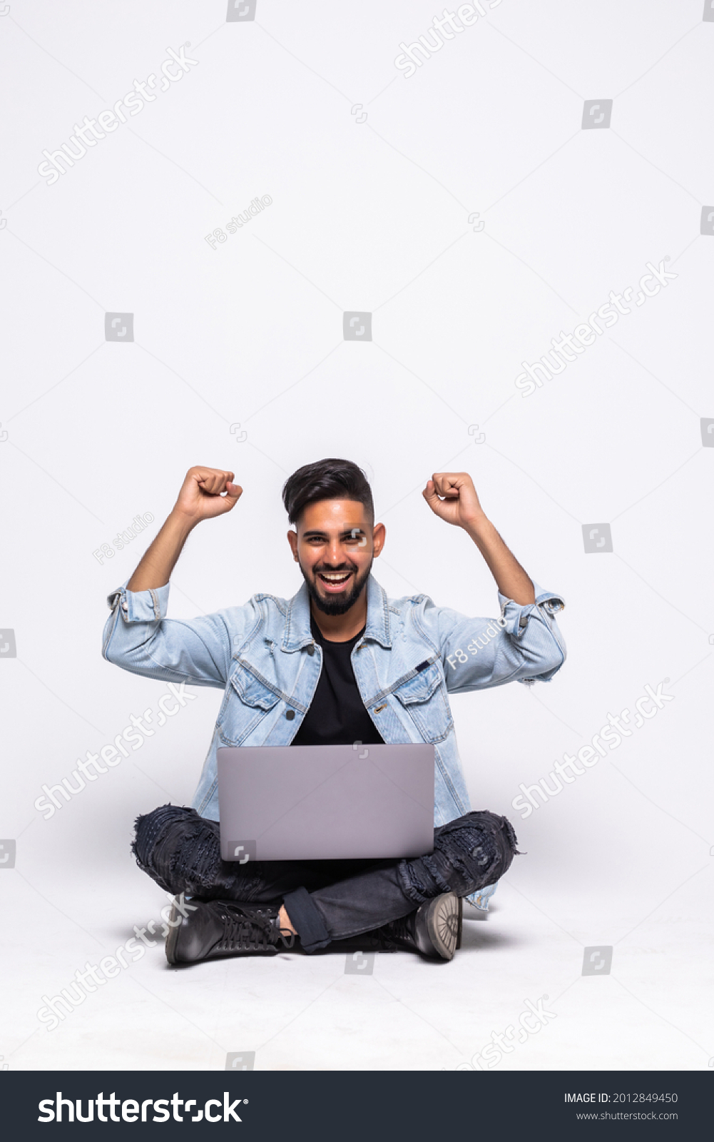 Happy man sitting on the floor with a laptop celebrate win isolated over a white background #2012849450