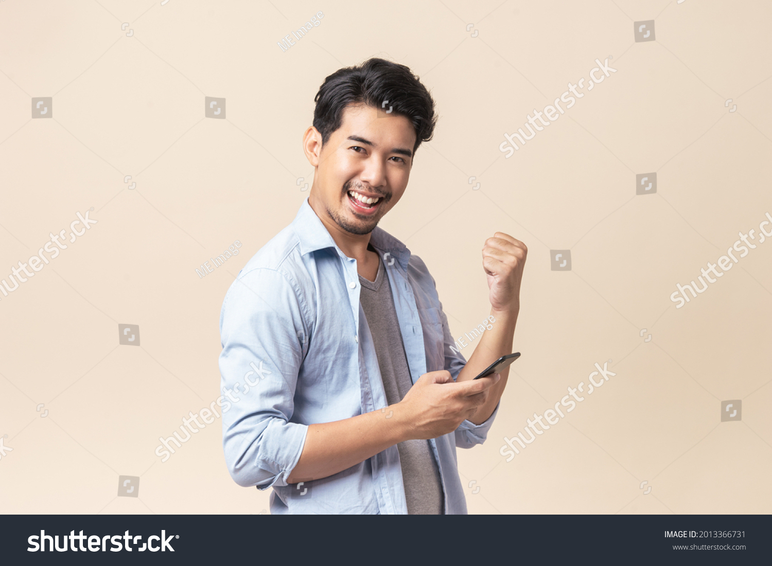 Portrait young Asian man handsome happy smile in formal shirt using smartphone trading or chatting on brown isolated studio background. #2013366731