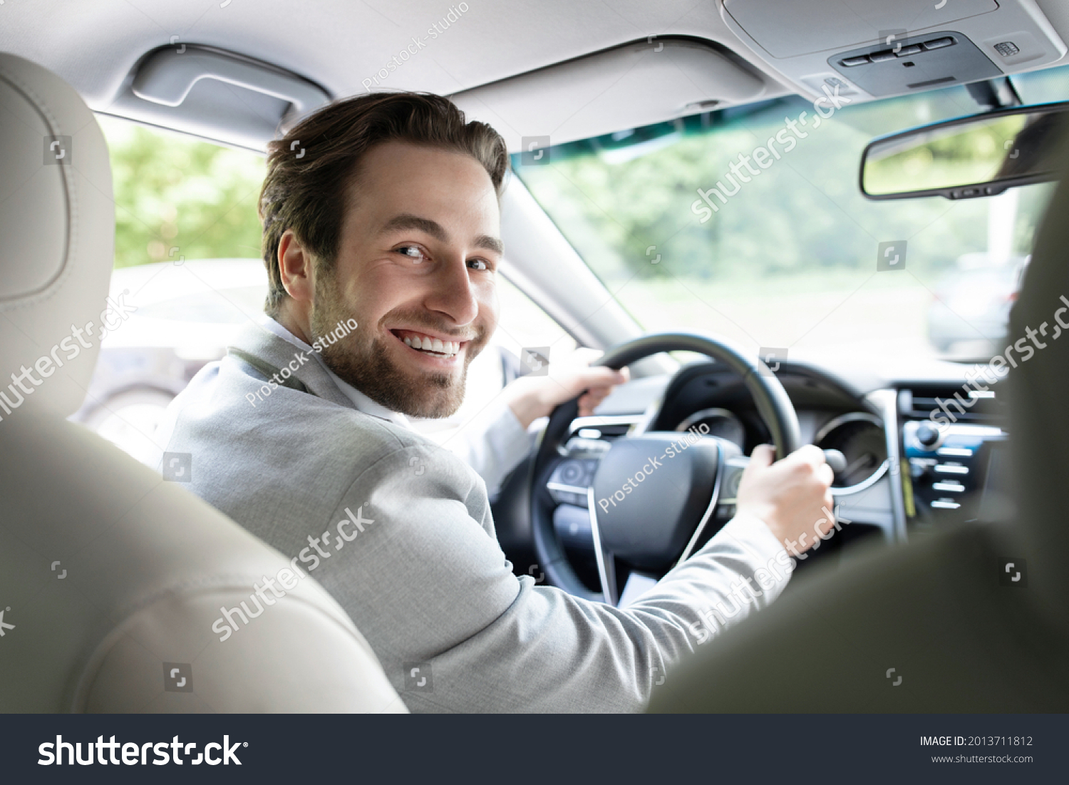 Lifestyle travel tourism positivity, transportation. Successful man sits at steering wheel of prestigious car. Portrait of handsome guy in suit, smiling driving auto, turns to passenger back seat #2013711812