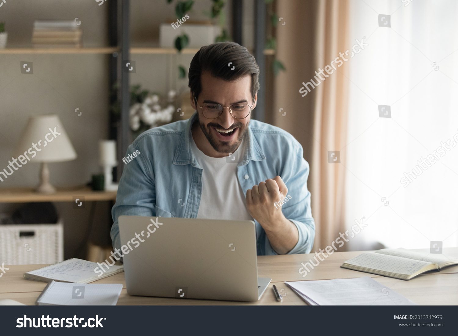 Man sit at desk read e-mail on laptop makes yes gesture feels happy. Male entrepreneur get great business news, celebrate career growth, advance. Achievement, win, moment of auction victory concept #2013742979