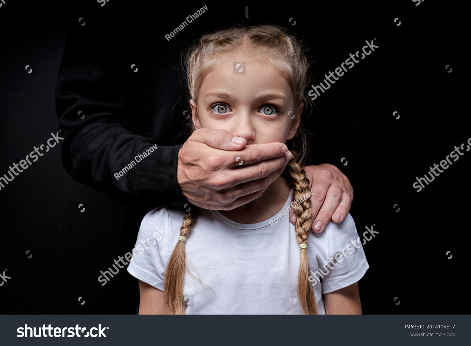 Scared girl with closed mouth by maniac killer, looking at camera with wide opened eyes, male hands on kid's shoulders, kidnapping, pedophile with child girl #2014114817