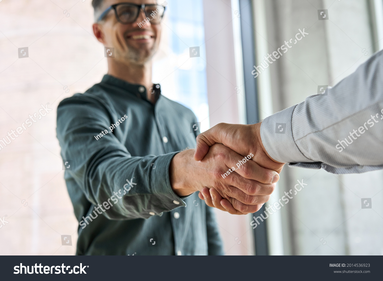 Two happy diverse professional business men executive leaders shaking hands at office meeting. Smiling businessman standing greeting partner with handshake. Leadership, trust, partnership concept. #2014536923