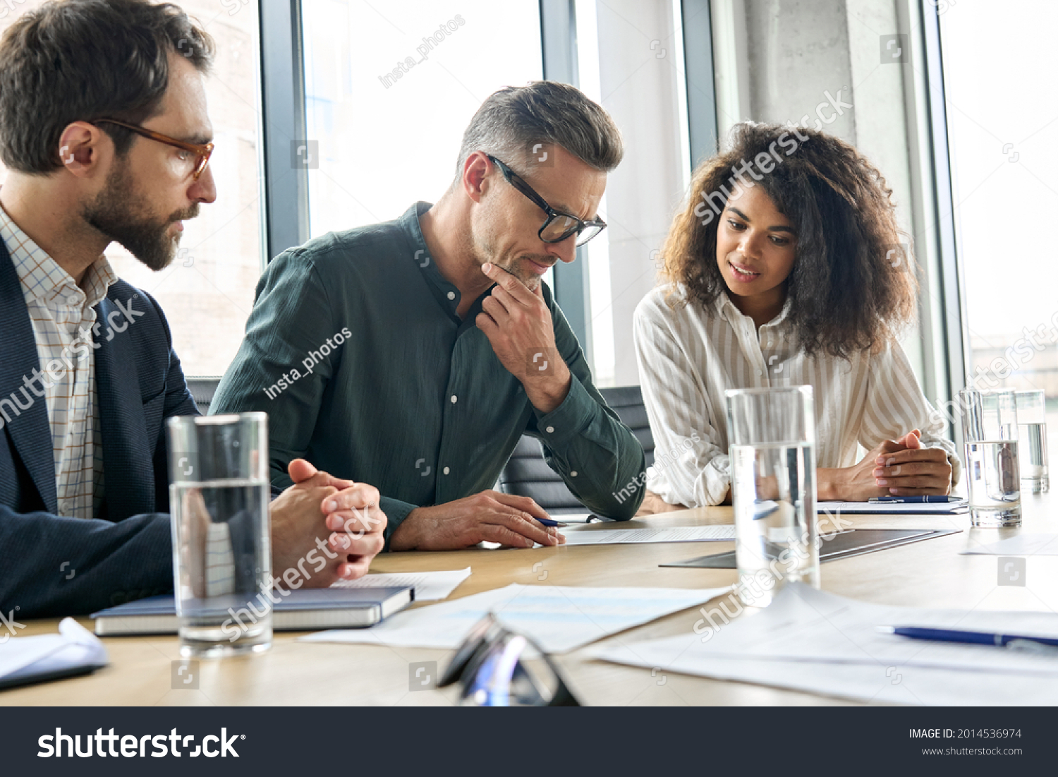 Focused doubtful mature businessman reading contract document thinking considering risks with professional lawyers legal experts executive team analyzing financial report sitting at office table. #2014536974