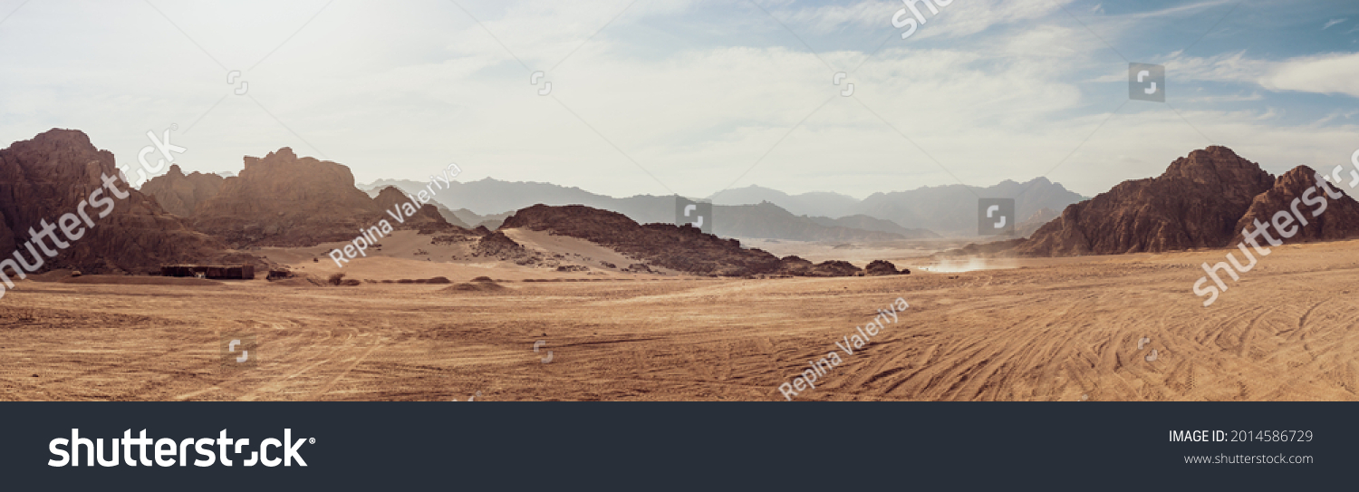 Safari and travel to Africa, extreme adventures or science expedition in a stone desert. Sahara desert at sunrise, mountain landscape with dust on skyline, hills and traces of the off-road car. #2014586729