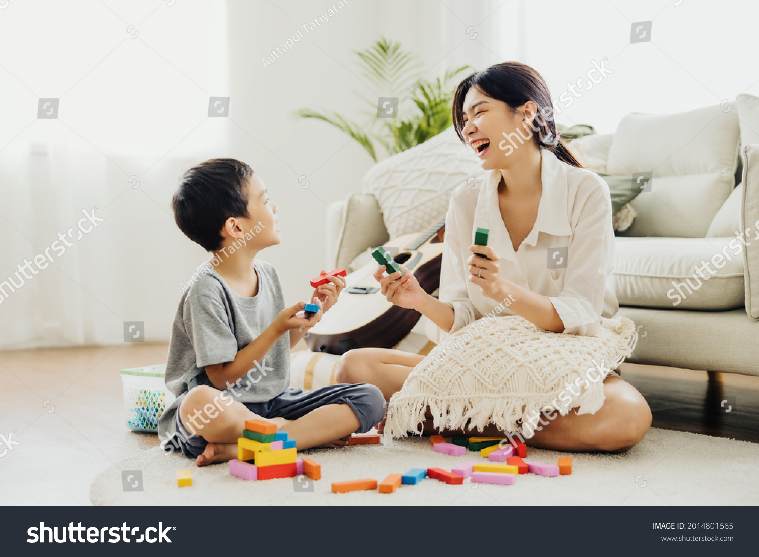 Cute Asian woman and kid playing educational toys together in living room. Mom and son play cubes and laugh Happy family. Young mother and son doing activities together at home. #2014801565