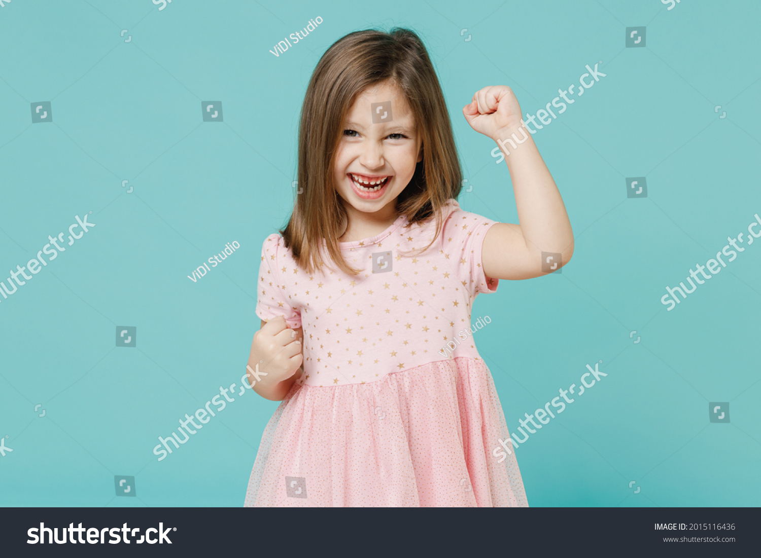 Little fun cute kid girl 5-6 years old wears pink dress doing winner gesture say yes isolated on pastel blue color background child studio portrait. Mother's Day love family people lifestyle concept #2015116436
