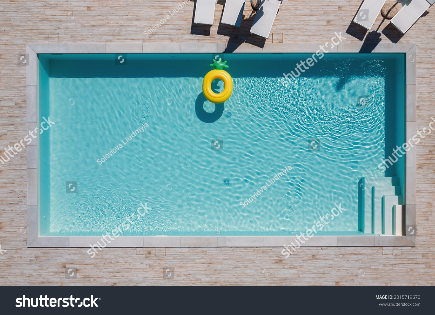 Empty rectangular blue swimming pool with sunbeds and umbrellas and big inflatable Yellow Pineapple floating tube. Rent a real estate or Chill out summer vacation in luxury resorts concept. #2015719670