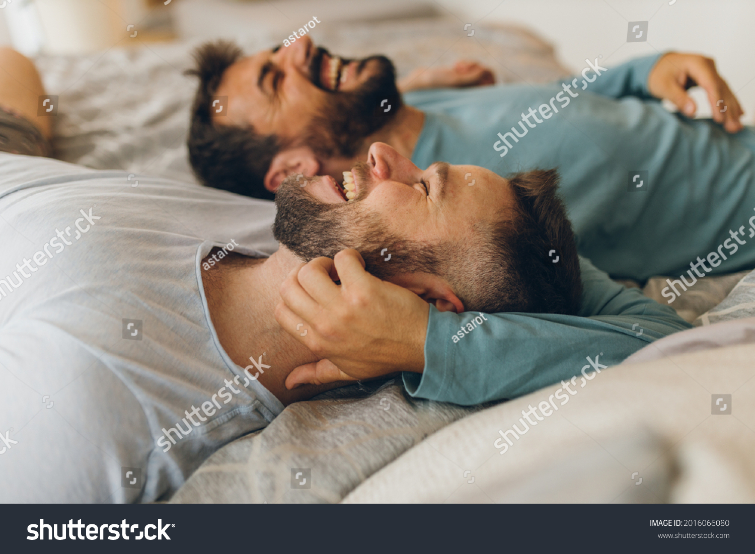 Happy gay couple lying down on the bed at home, hugging and flirting. #2016066080