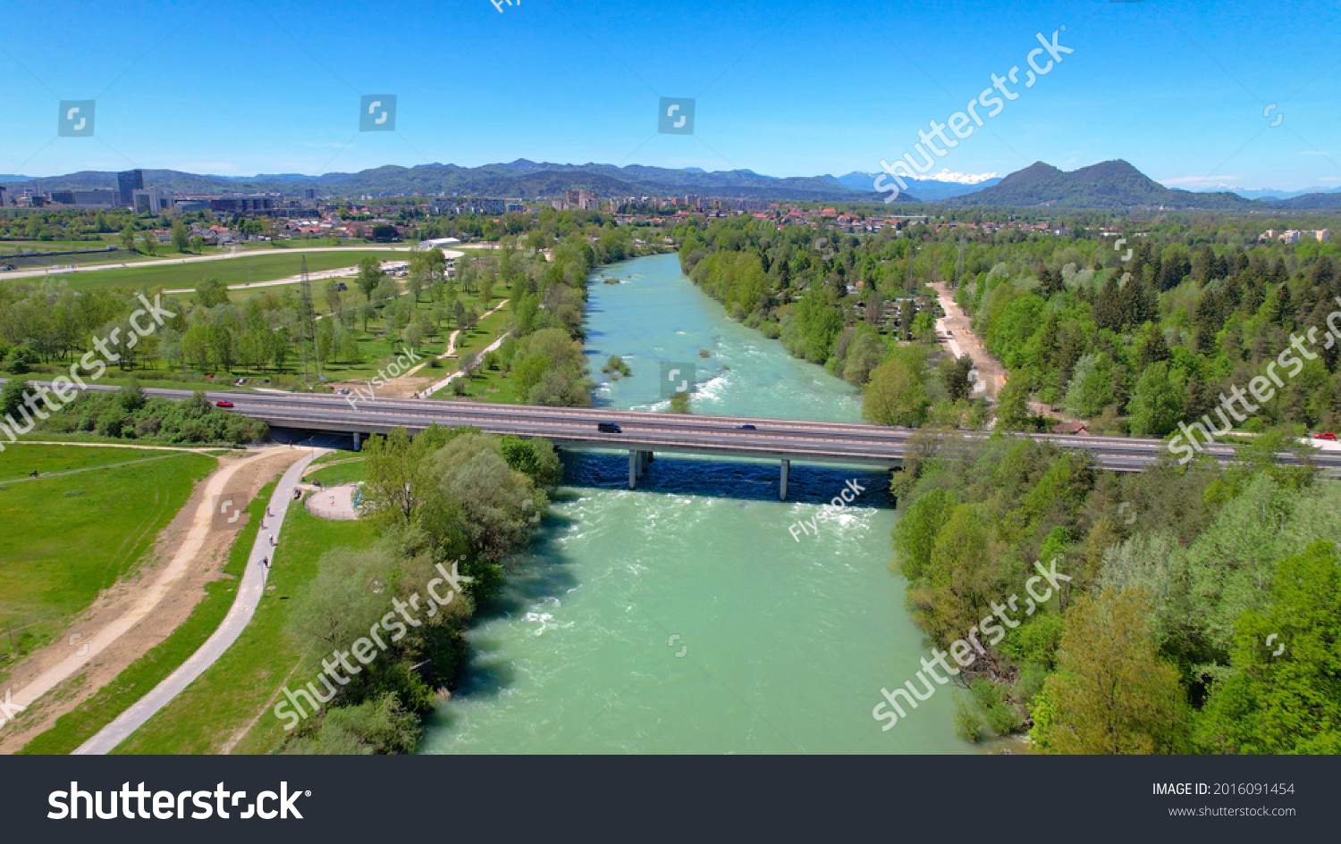 AERIAL: Scenic drone point of view of a highway crossing the emerald river crossing the lush green Slovenian landscape. Sava river coursing through the vibrant Ljubljana suburbs on sunny summer day. #2016091454