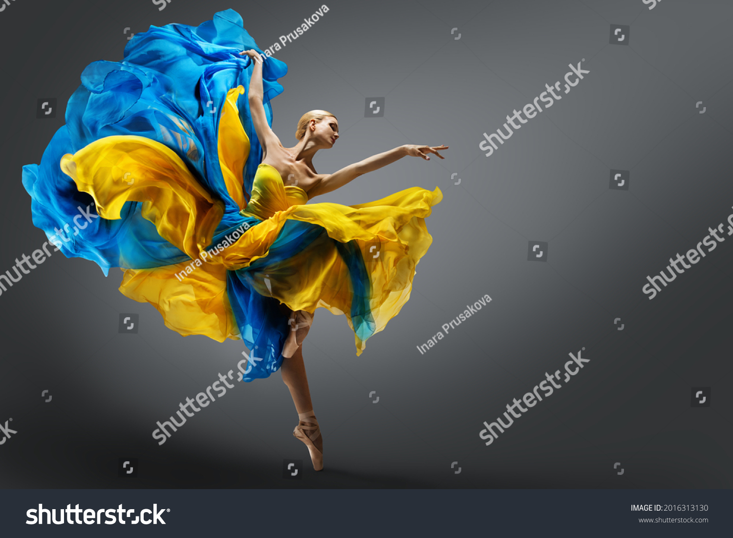 Beautiful Woman Ballet Dancer Jumping in Air in Colorful Fluttering Dress. Graceful Ballerina Dancing in Yellow Blue Gown over Gray Studio Background #2016313130