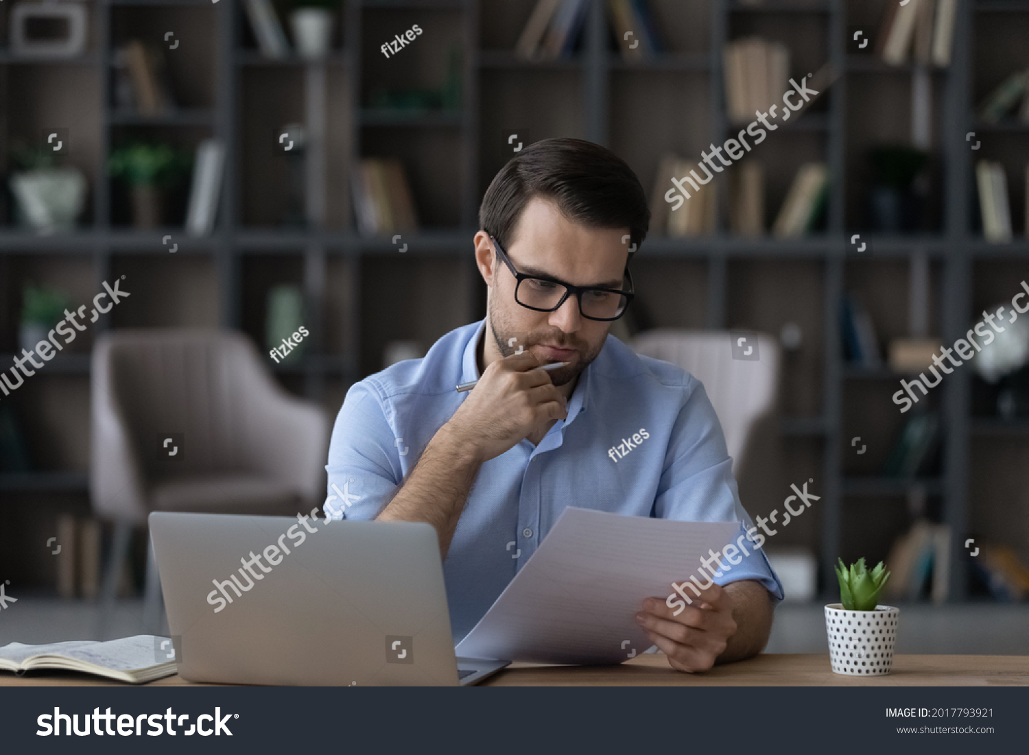 Working with papers. Serious millennial male entrepreneur work at home office alone hold read document hardcopy think on conditions terms. Focused young man engaged in paperwork edit text of agreement #2017793921