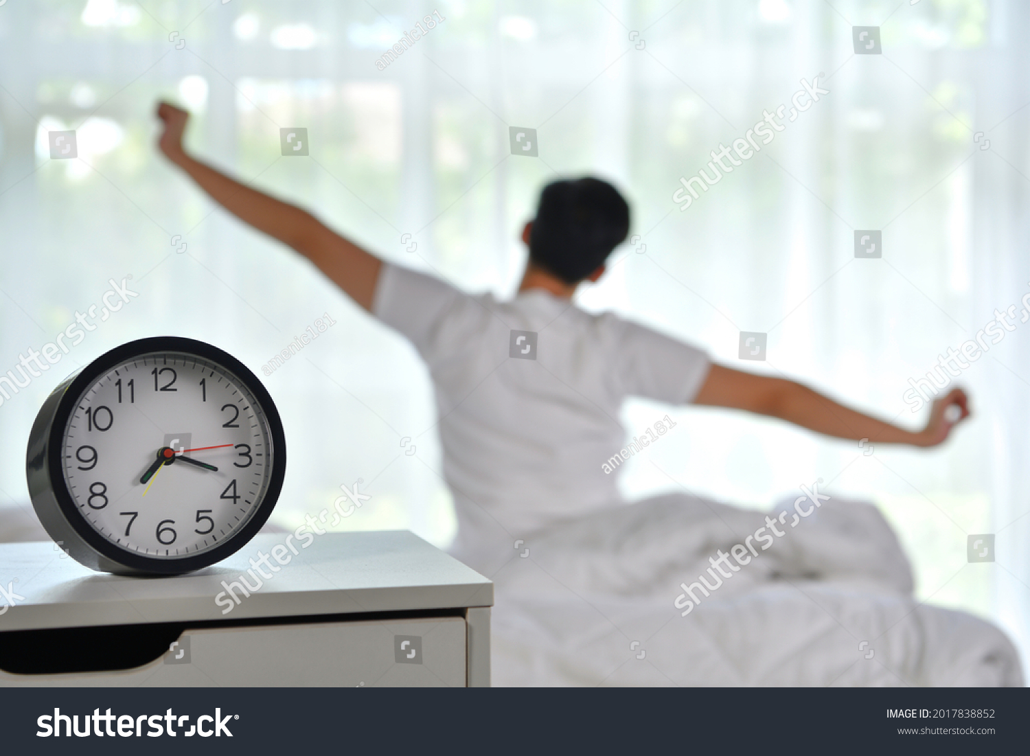 Man waking up in the morning sitting on bed and stretching, focus on alarm clock #2017838852