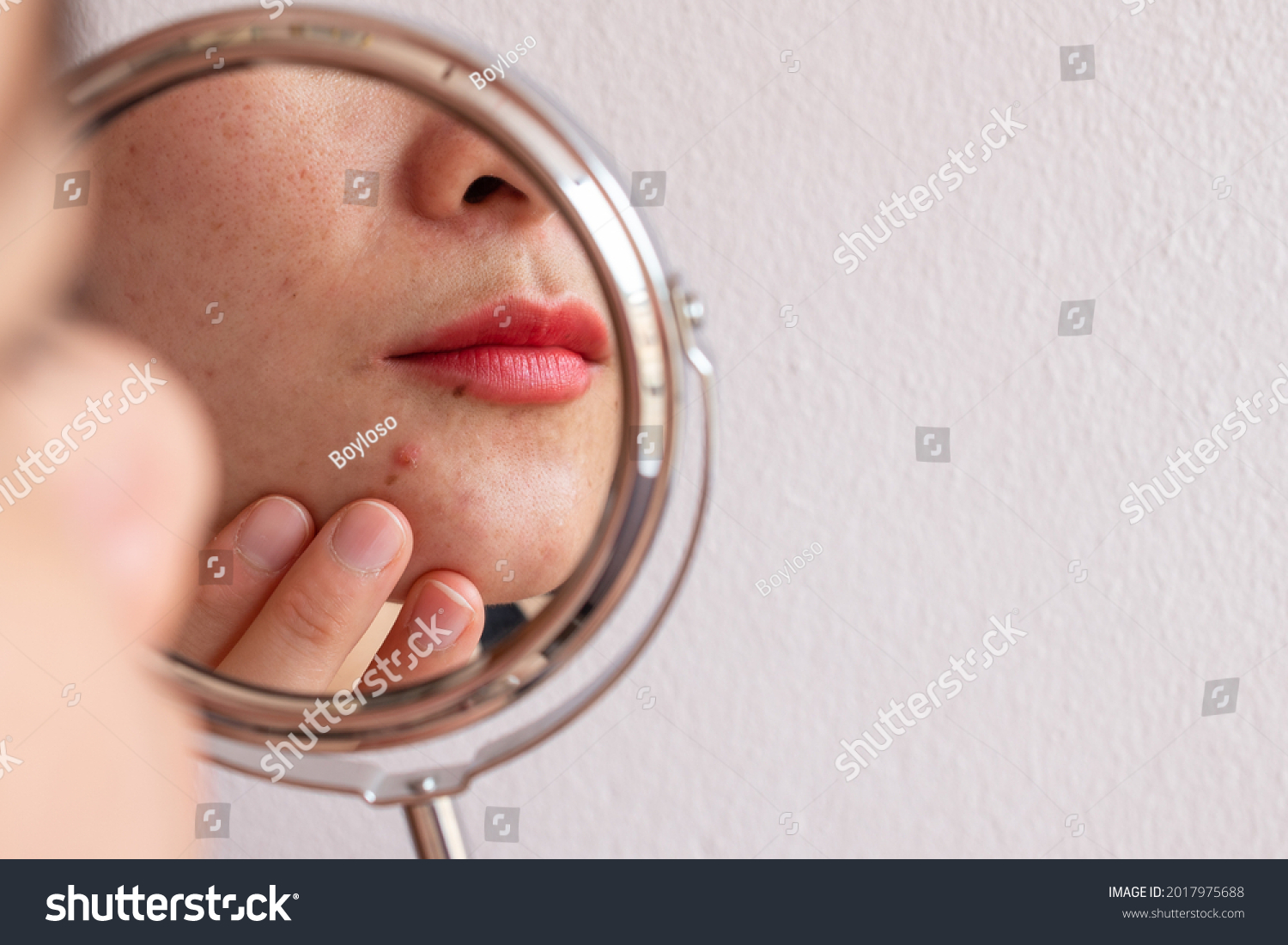 Cropped shot of woman worry about her face when she saw the problem of acne occur on her chin by a mini mirror. Conceptual shot of Acne and problem skin on female face. #2017975688
