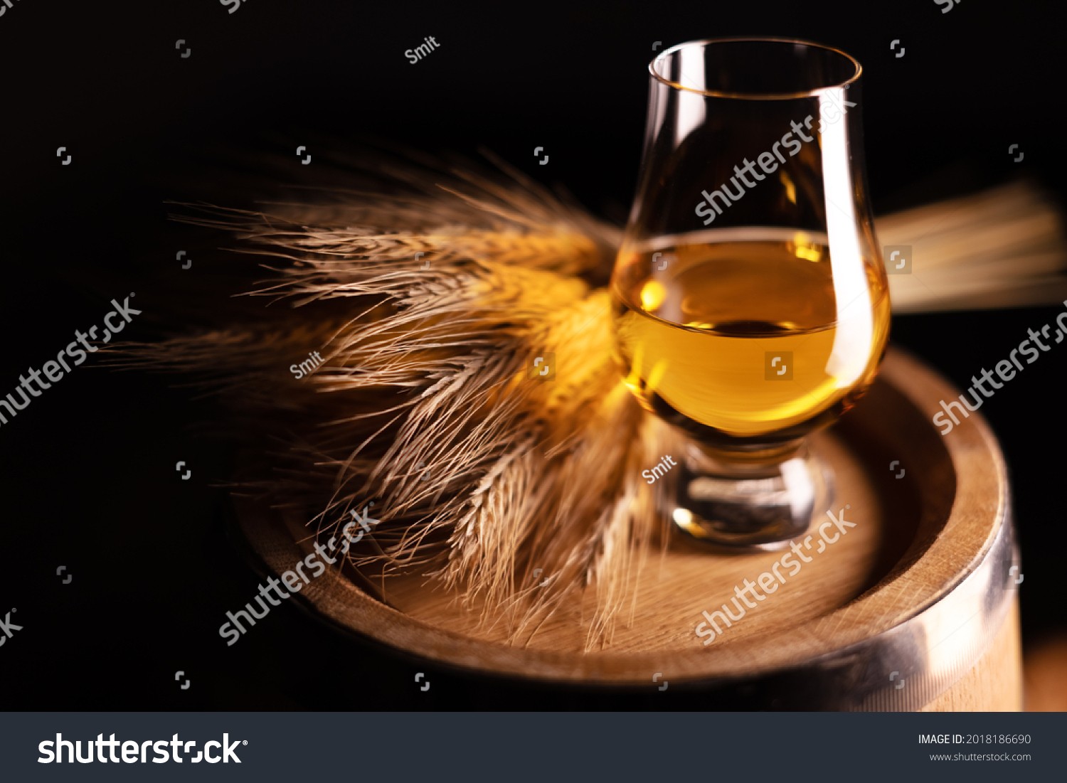 A glass of whiskey on old oak barrel with bunch of rye. Traditional alcohol distillery concept #2018186690