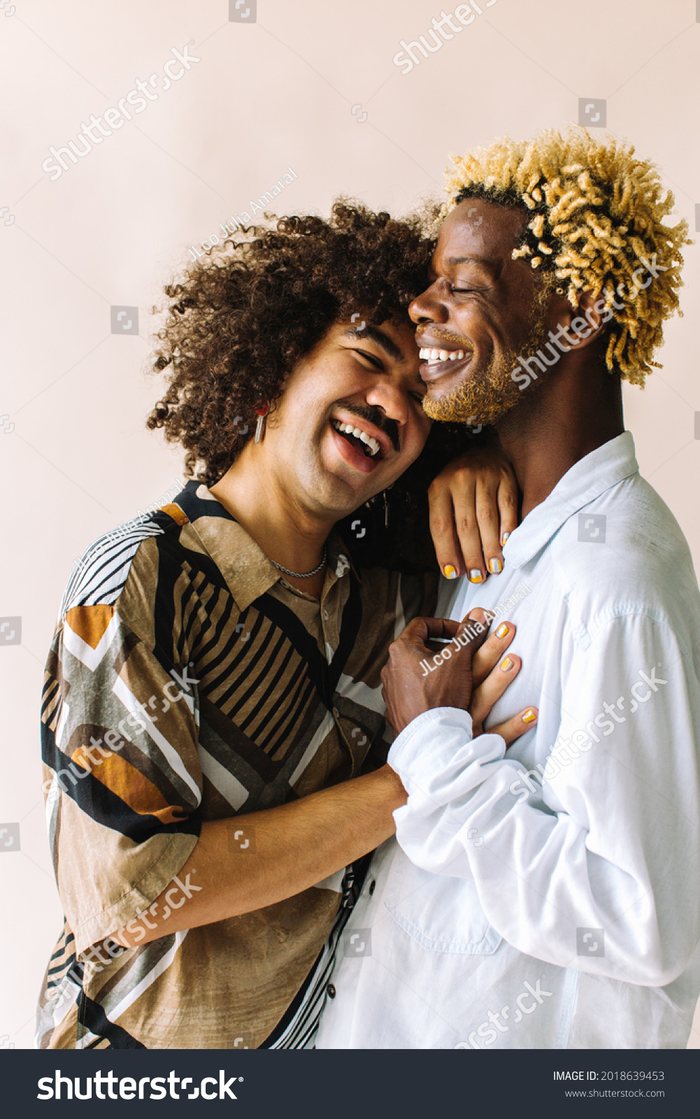 Carefree young gay couple standing together in a studio. Two affectionate male lovers smiling cheerfully while embracing each other against a studio background. Young gay coupe being romantic. #2018639453