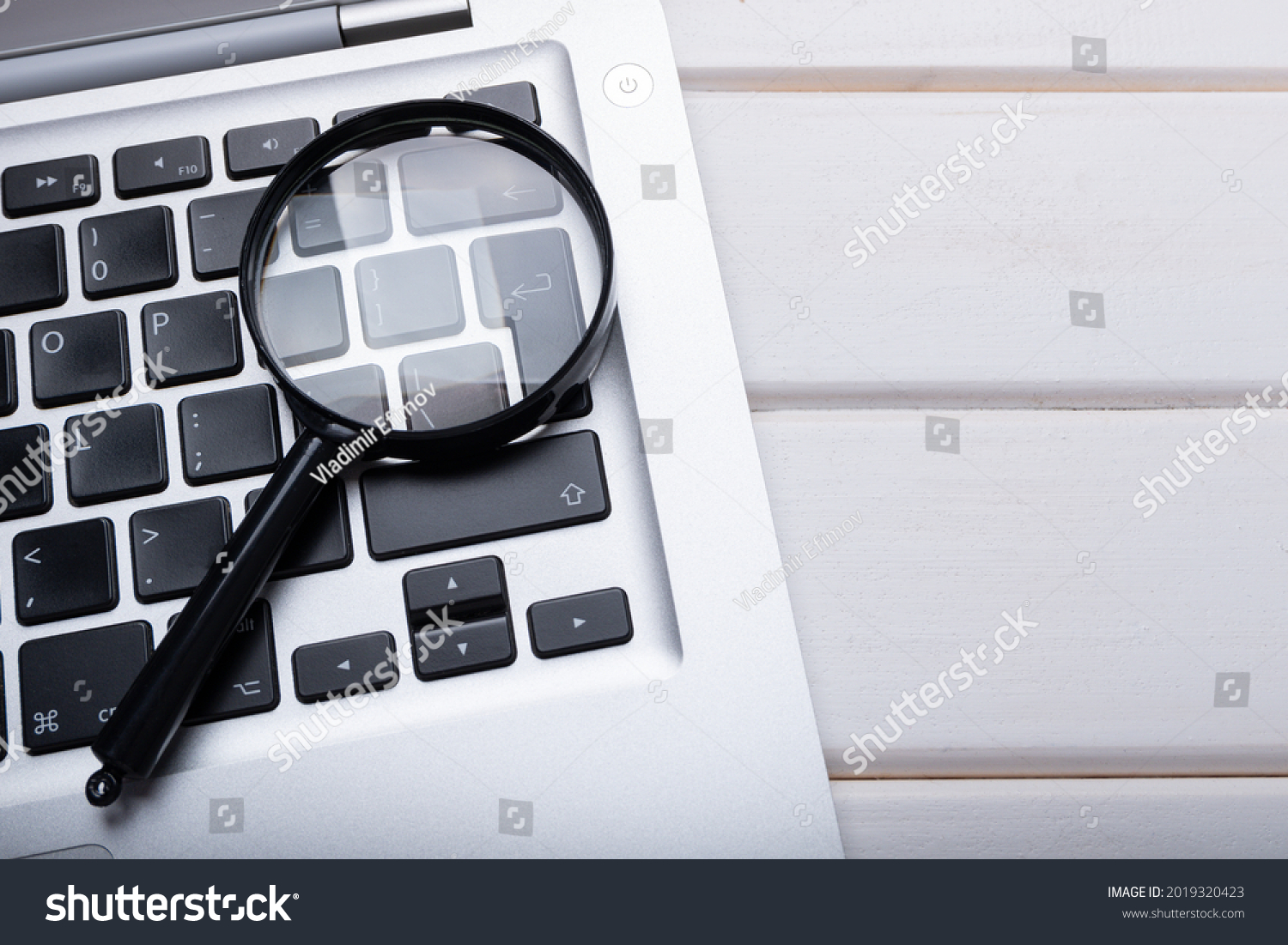 Magnifying glass laying on a laptop keyboard. Technology file search tool concept, data forensics, computer crime and device investigation, closeup #2019320423