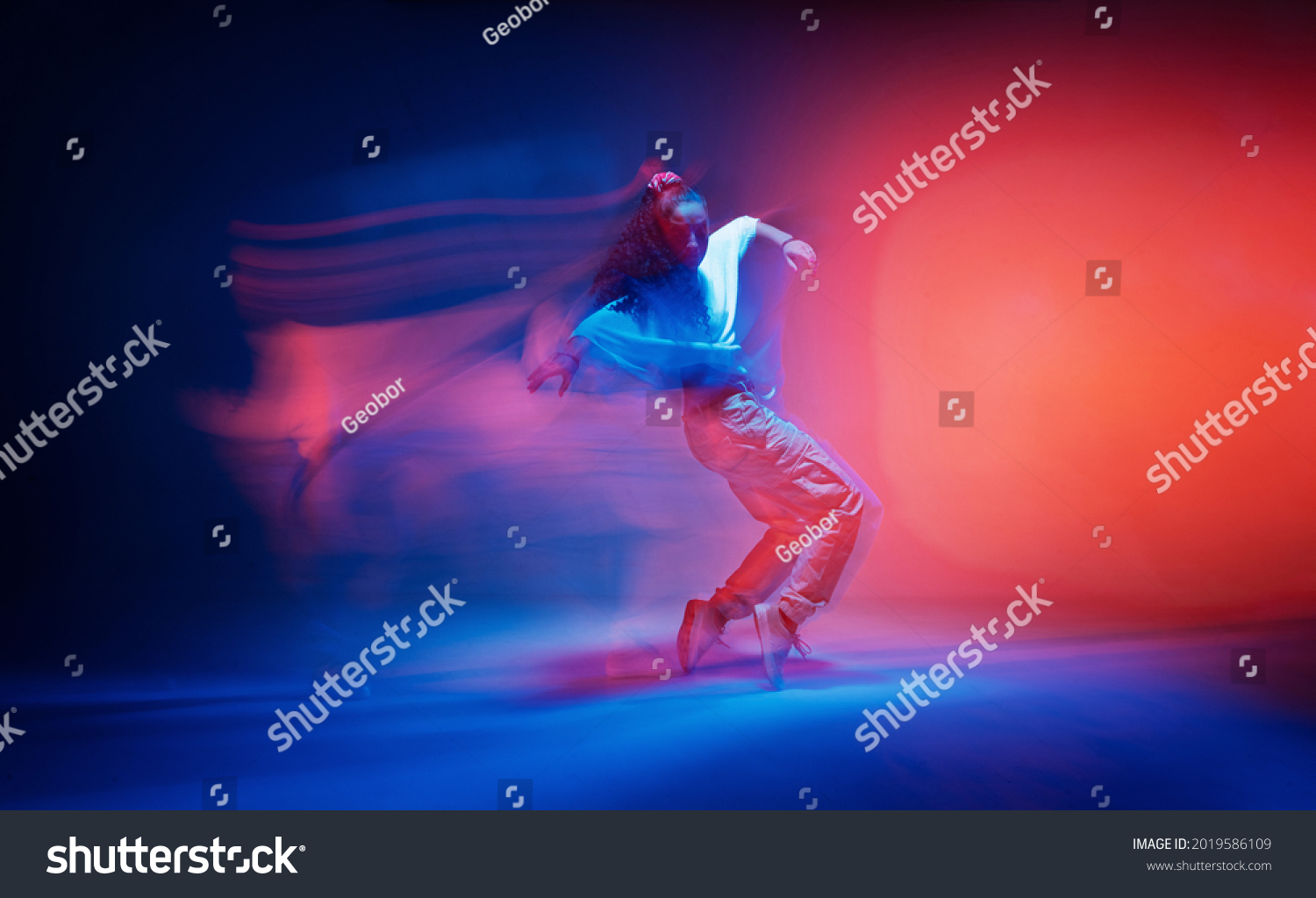 Dancing female standing on tiptoe in colourful neon studio light. Long exposure. Contemporary hip hop dance #2019586109