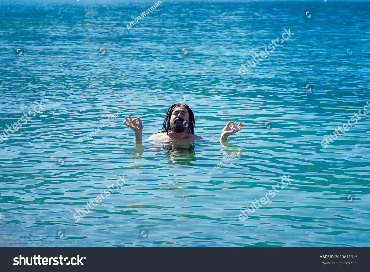 A man with dreadlocks in a relaxed Om position in turquoise water. Relaxation and enlightenment. #2019611315