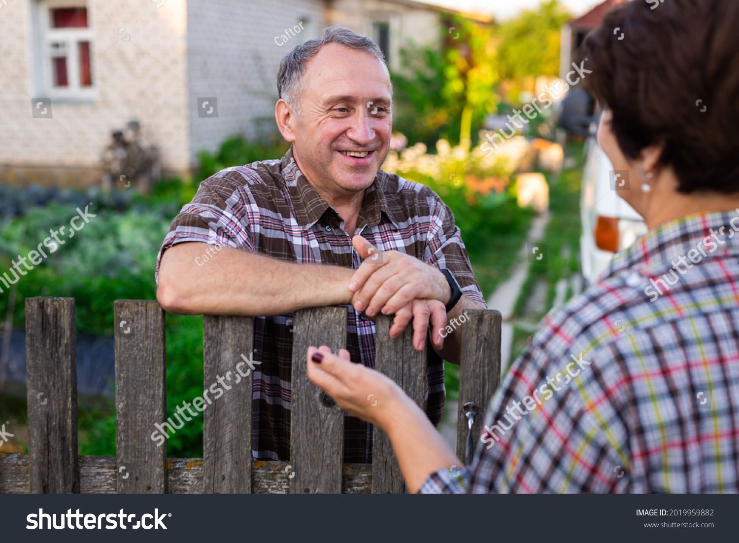 neighbors middle aged man and woman chatting near the fence in the village #2019959882