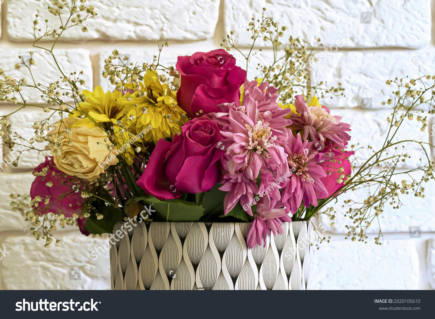 A fading bouquet of flowers on a white brick wall background. A bouquet of multi-colored drying flowers. Details of the texture of fading petals. Beauty of nature. Faded life concept #2020105610