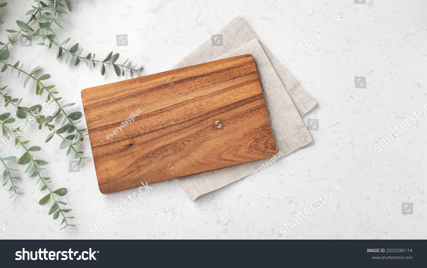 Wood cutting board with linen napkin and plant on marble table with copy space, top view #2020286114