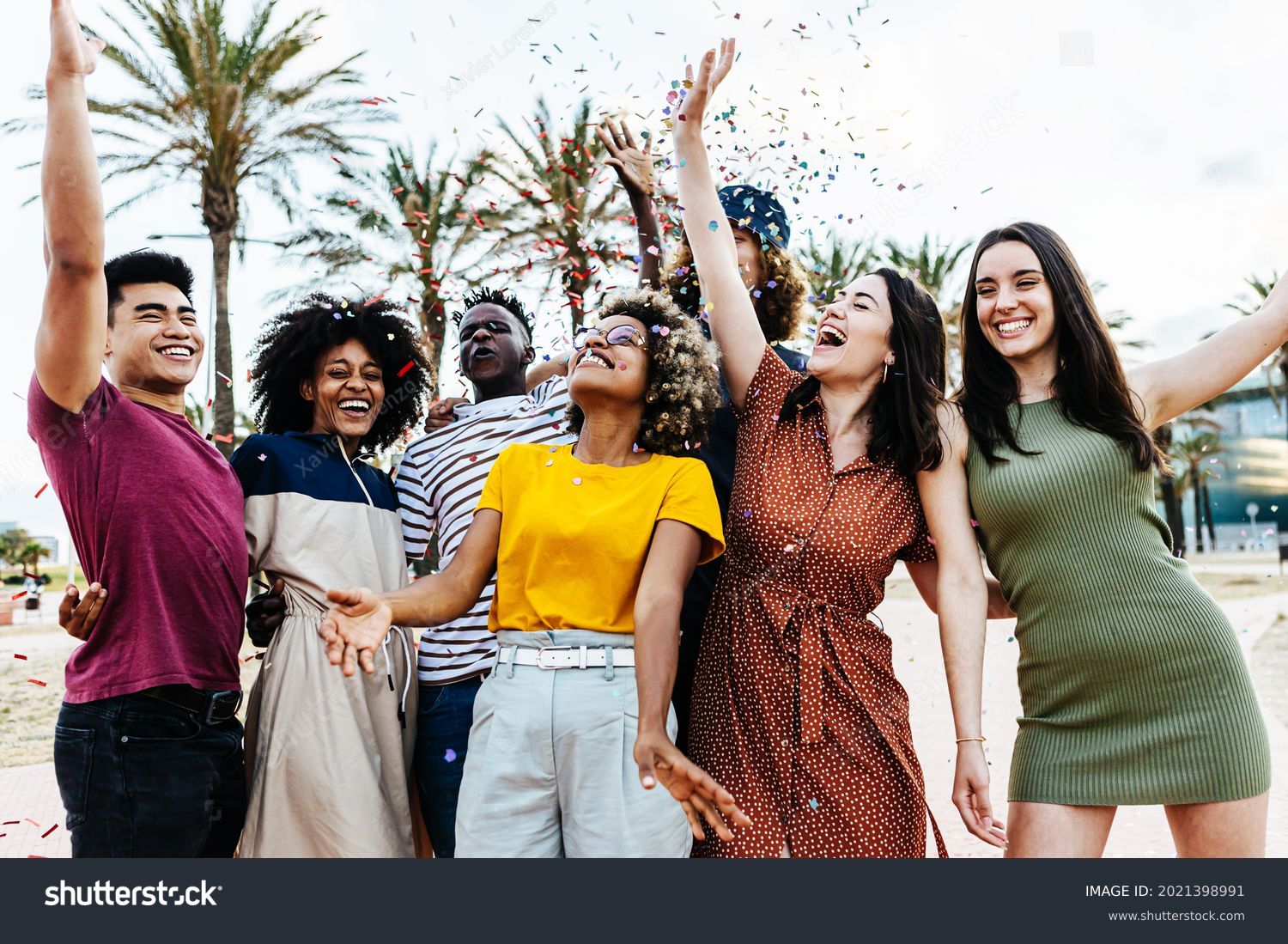Young multiracial hipster people having fun in summer party celebration - Group of young friends laughing and celebrating all together while throwing coloured confetti at weekend event outdoors #2021398991