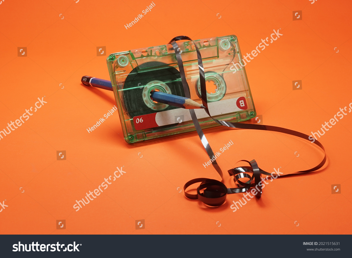 Crumpled cassette tape being rolled using blue pencil on isolated orange background                       #2021515631