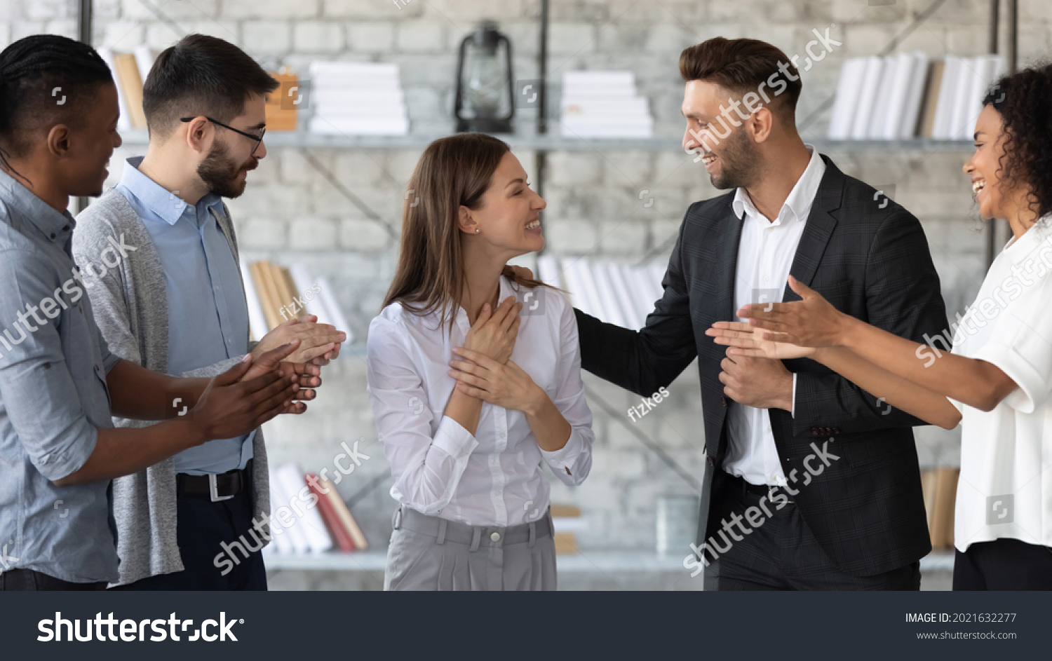 Smiling supportive diverse businesspeople congratulate excited young Caucasian female employee with job promotion or success. Happy multiethnic colleagues greeting woman worker with work achievement. #2021632277