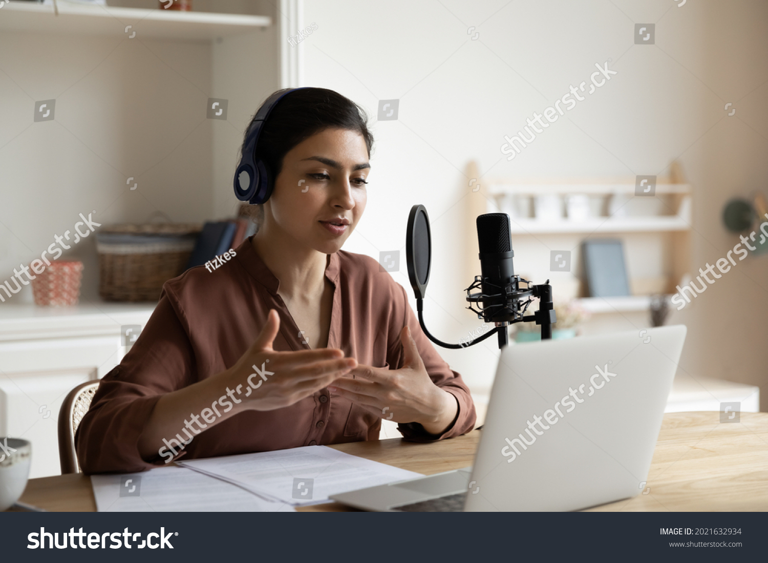 Young Indian female coach or trainer use headphones microphone record live podcast vlog talk on video call on computer. Ethnic female have webcam digital virtual event on laptop. Technology concept. #2021632934