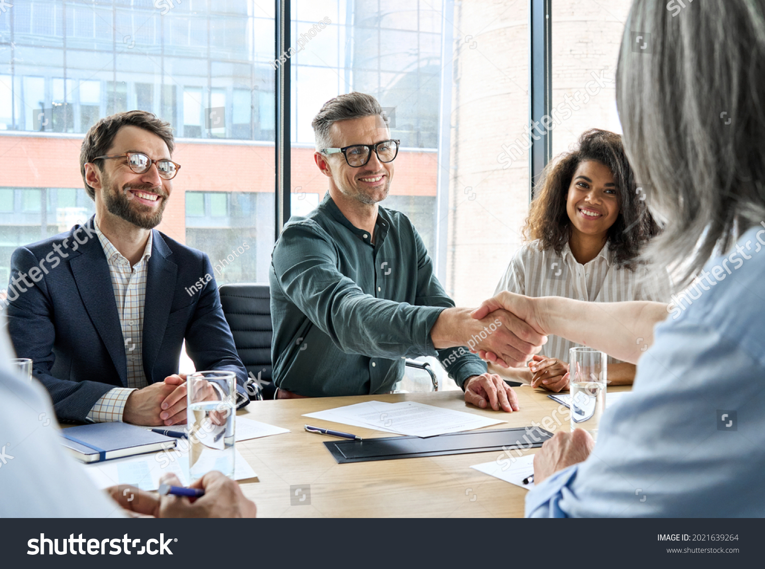 Happy businessman and businesswoman shaking hands at group board meeting. Professional business executive leaders making handshake agreement successful company trade partnership handshake concept. #2021639264