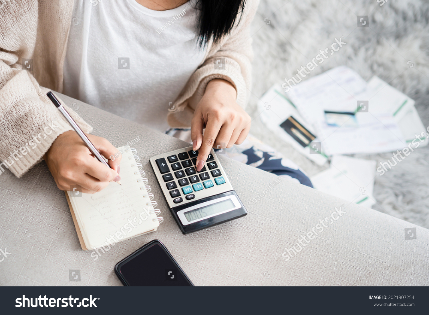 woman writing a list of debt on notebook calculating her expenses with calculator with many invoices , female hand doing accounting  #2021907254