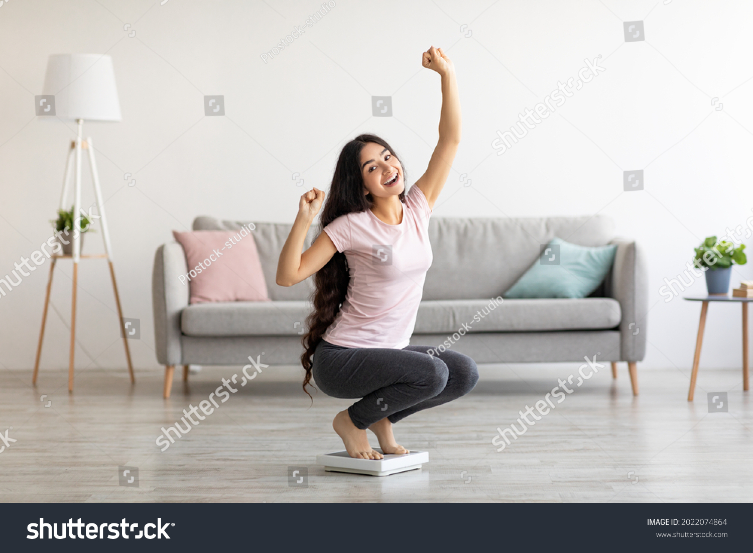 Overjoyed Indian woman sitting on scales, gesturing YES, excited over result of her weight loss diet at home. Millennial Asian lady achieving her slimming goal, copy space #2022074864