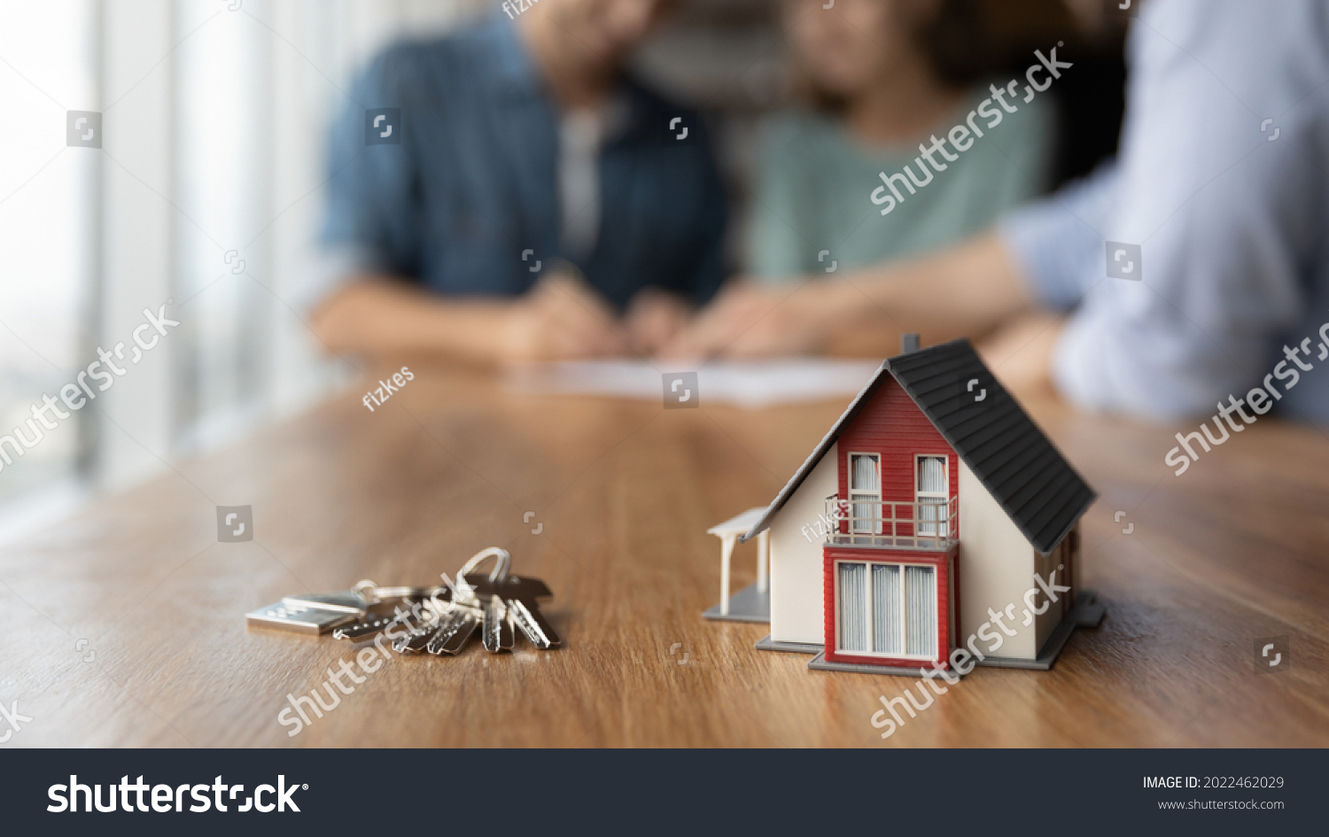 Close up of key and tiny toy house on table. Married couple buying house, consulting, lawyer, legal advisor, real estate agent, bank manager, signing mortgage agreement in background #2022462029