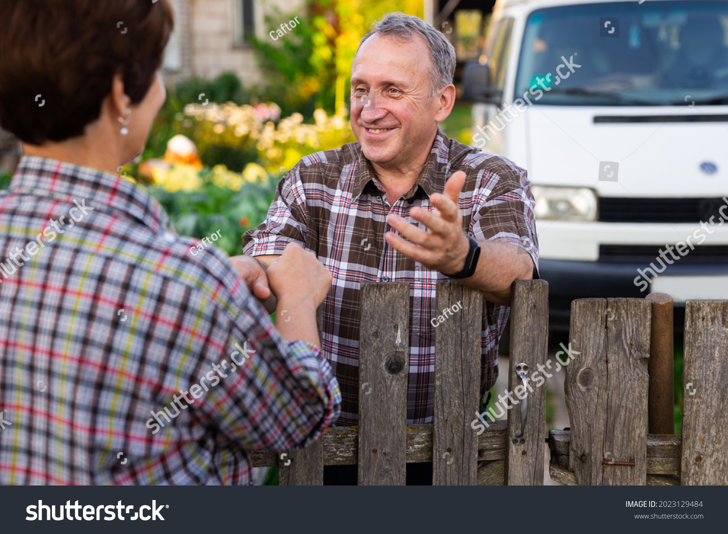 neighbors middle aged man and woman chatting near the fence in the village #2023129484