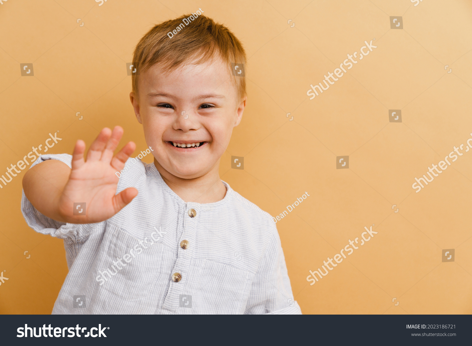 White boy with down syndrome smiling and gesturing at camera isolated over beige background #2023186721