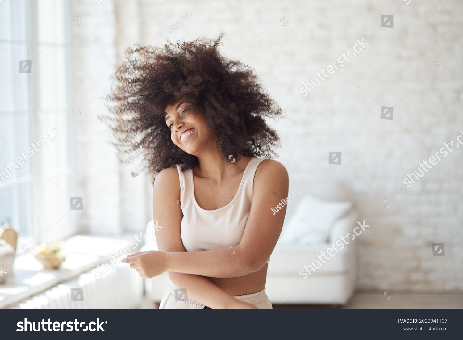 A satisfied mixed-race woman enjoys rhythmic movement. A cheerful young black lady dancing and enjoying a carefree weekend at home while relaxing in her apartment, listening to music, no stress. #2023341107
