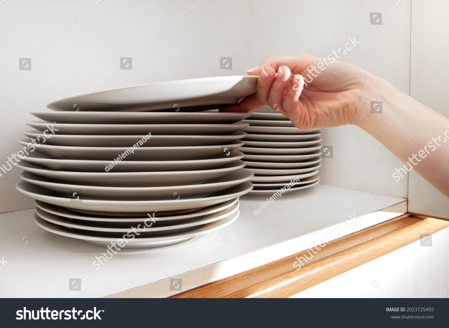 Fingers picking up a plate from a stack in the cupboard #2023725455