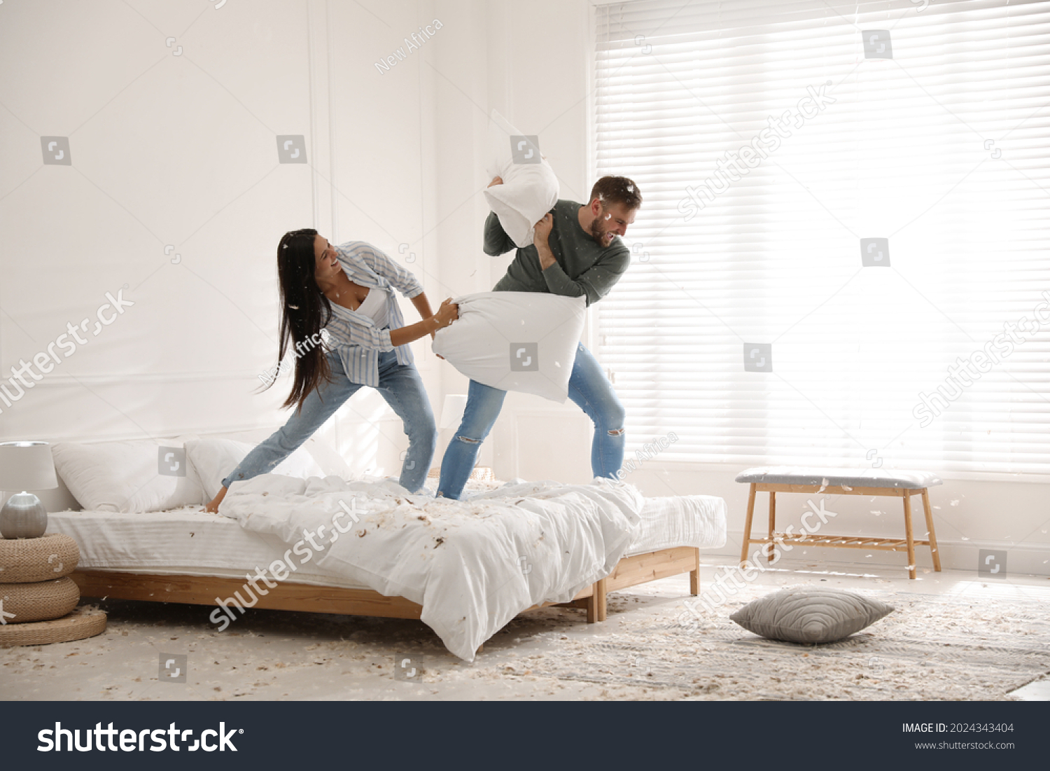 Happy young couple having fun pillow fight in bedroom #2024343404