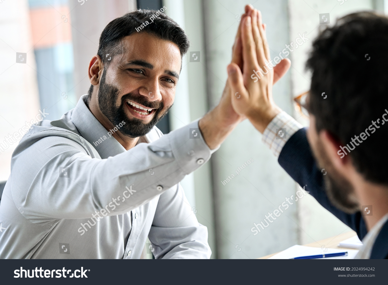 Indian happy smiling multiracial professional ceo businessman giving highfive to business partner after financial acquisition bank bargain contract at office. High five concept. Over shoulder view. #2024994242