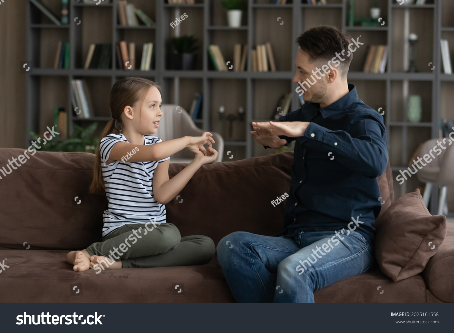 Little 7s deaf girl her father sit on couch speaking without words showing visual manual gestures using symbols. Professional speech therapist teach child. hearing impairment, communication concept #2025161558