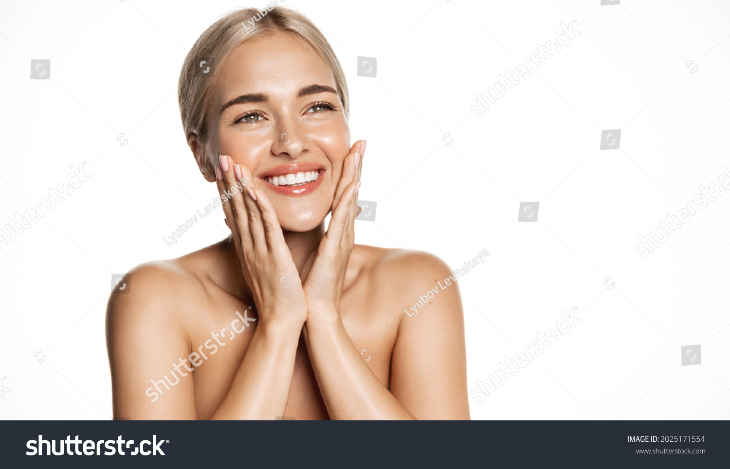 Spa and cosmetology. Young blond woman smiling happy, looking up, holding hands on face, apply moisturizing cream, face lotion or toner, white background #2025171554