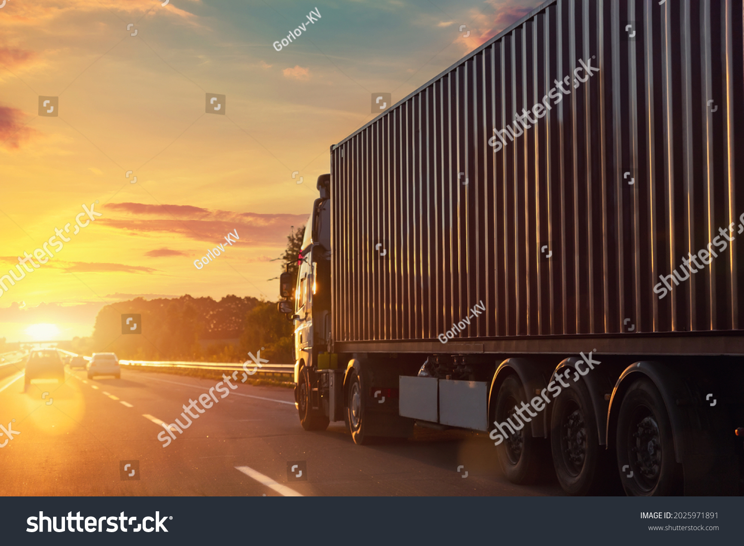 Scenic front view big long heavy semi-treailer truck with sea shipping container driving highway dramatic warm morning evening sunrise sun sky sunset. Cargo transport industry background concept #2025971891