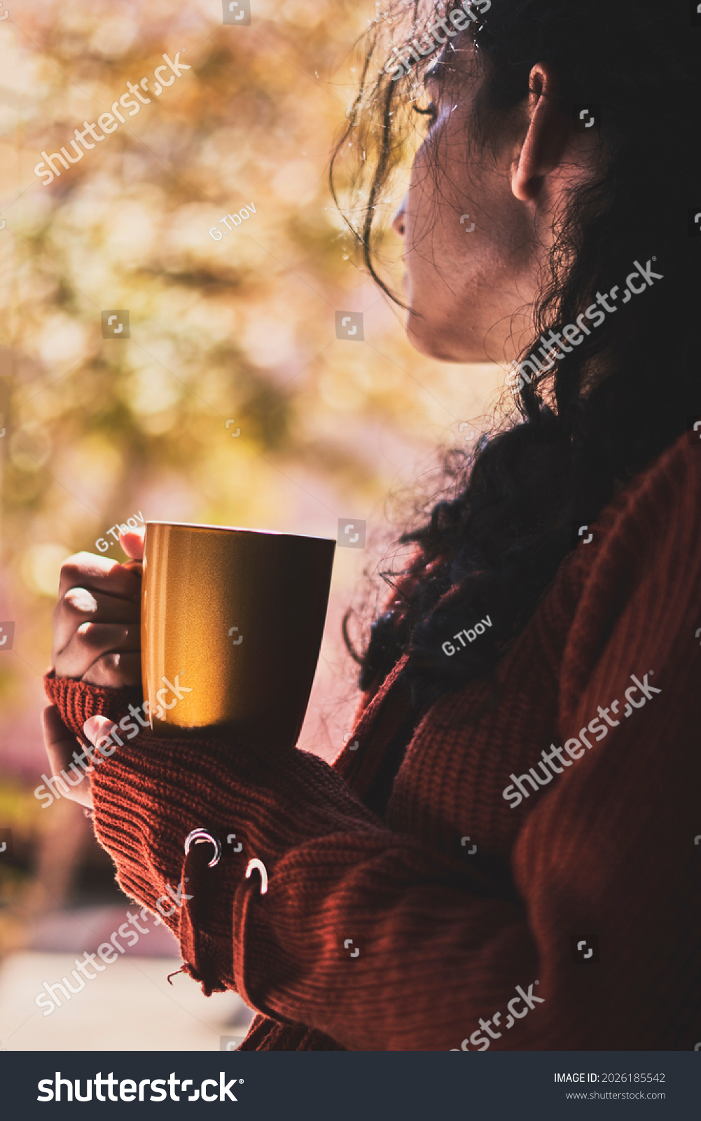 Cold autumn days - a young multi-racial female drinks coffee in a cozy windowsill. Middle-eastern or mixed-race woman enjoys weekend drinking hot tea near the windows #2026185542