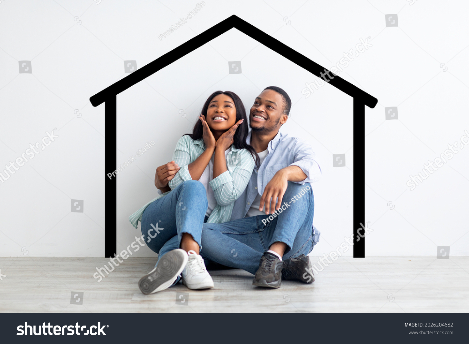 Happy african american spouses sitting near white wall with drawn house, dreaming and imagining their new home, planning relocation, creative collage #2026204682