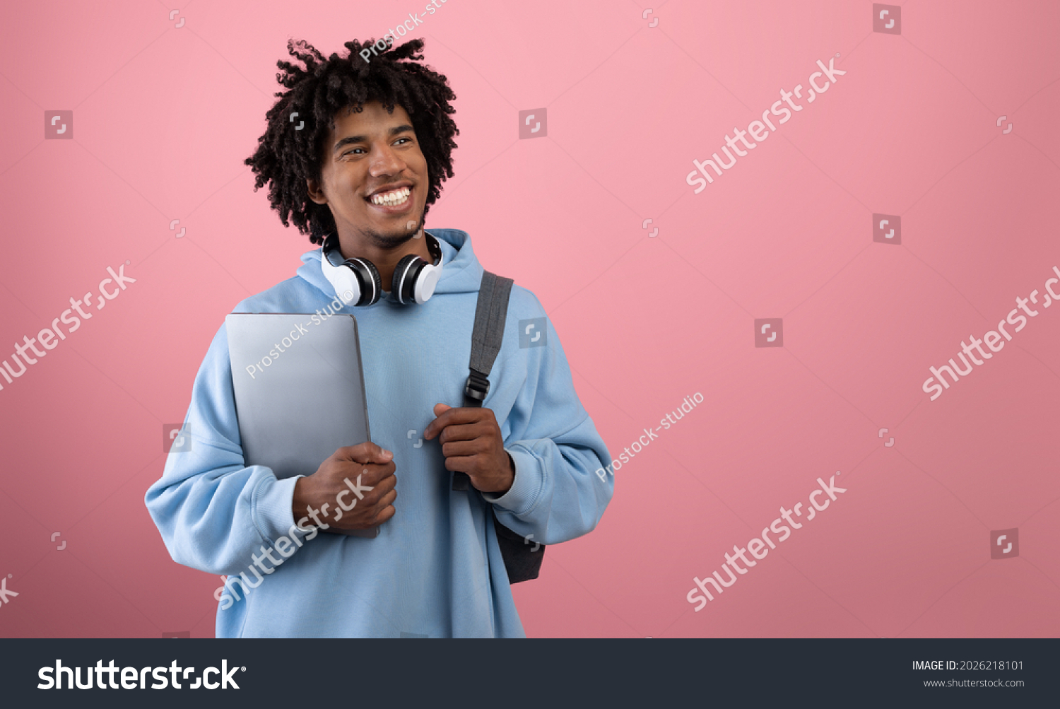 Positive African American teen student with backpack, tablet pc and headphones studying online on pink studio background, banner with free space. Happy black adolescent having remote college education #2026218101