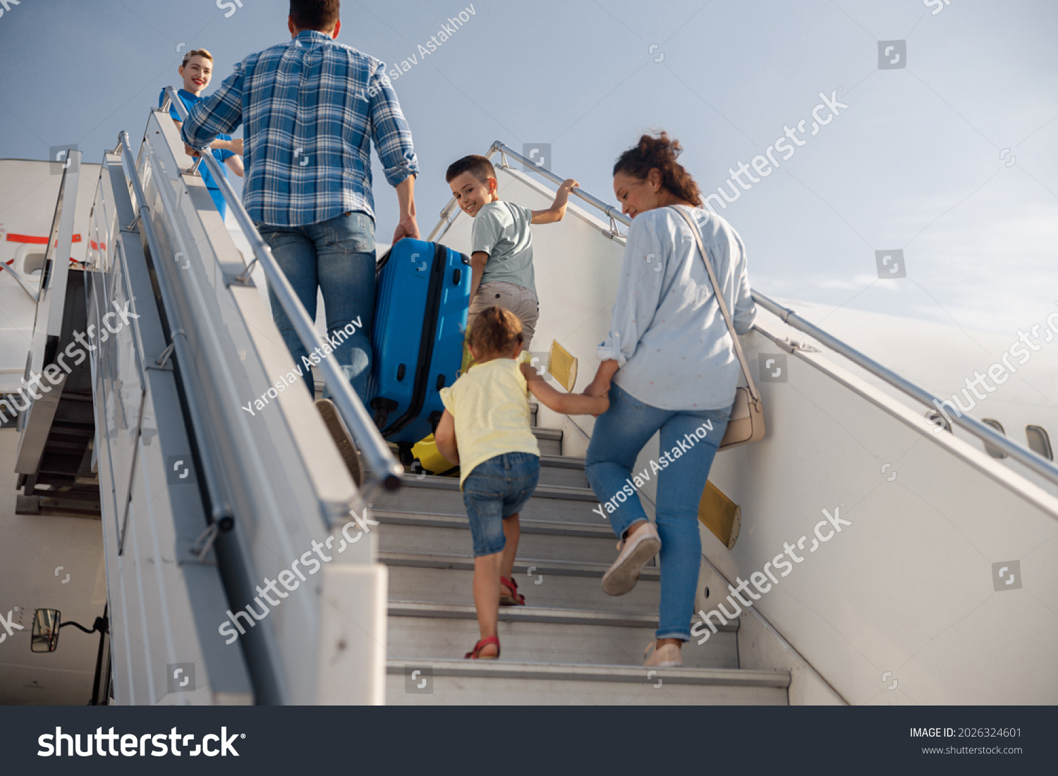 Back view of parents with two kids getting on, boarding the plane on a daytime, ready for summer vacations. People, traveling, vacation concept #2026324601